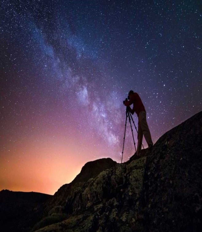Homem nas montanhas a observar as estrelas com um telescópio à noite
