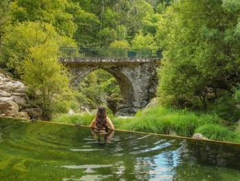 mulher dentro de água numa ribeira a contemplar a paisagem florestal