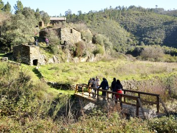 pessoas a caminhar numa ponte junto a umas ruínas de pedra