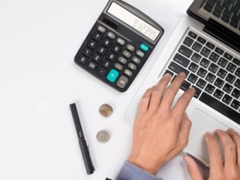 mesa de escritório com calculadora, caneta moedas e computador